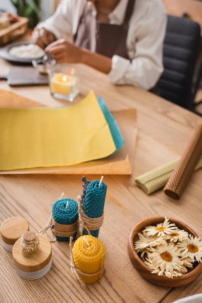 Camomille essiccate e candele fatte in casa vicino a fogli di cera e ritagliato artigiana afro-americana su sfondo sfocato — Foto stock