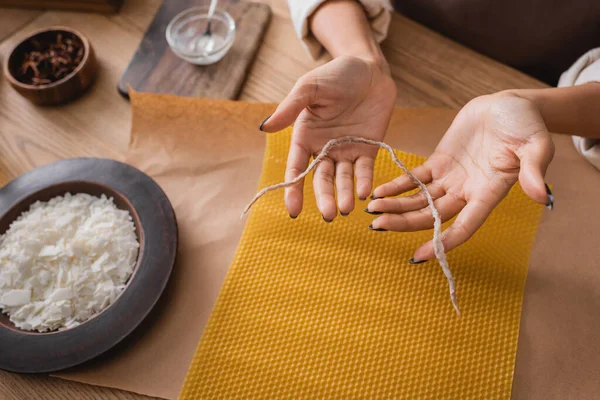 Partial view of african american woman holding twine near wax sheet and wooden plate with grated beeswax in workshop — Stock Photo