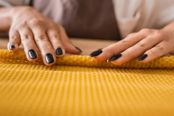 Partial view of african american craftswoman with manicure rolling wax sheet while making natural candle in workshop — Stock Photo
