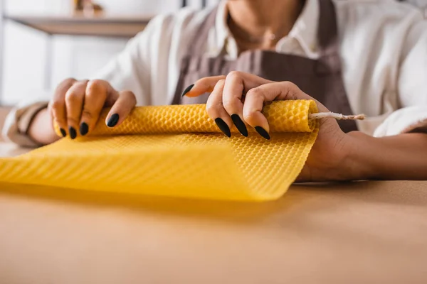 Partial view of blurred african american woman making candle and rolling wax sheet in craft workshop — Stock Photo