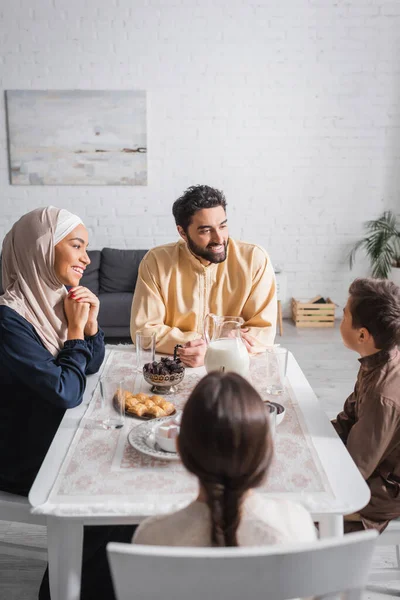 Famille musulmane souriante parlant près de la nourriture pendant le ramadan à la maison — Photo de stock
