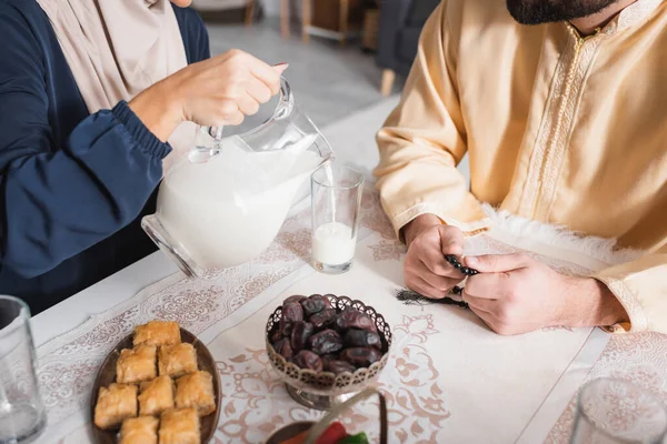 Cropped view of muslim woman pouring milk near husband during suhur at home — Stock Photo