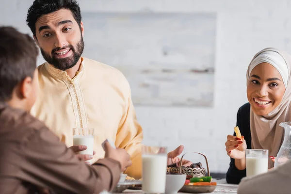 Smiling muslim parents talking to son near suhur food at home - foto de stock