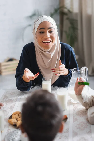 Smiling african american mother in hijab talking to kids during suhur breakfast at home — Foto stock