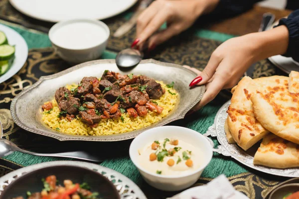 Cropped view of muslim woman putting pilaf on table during iftar at home — Stock Photo