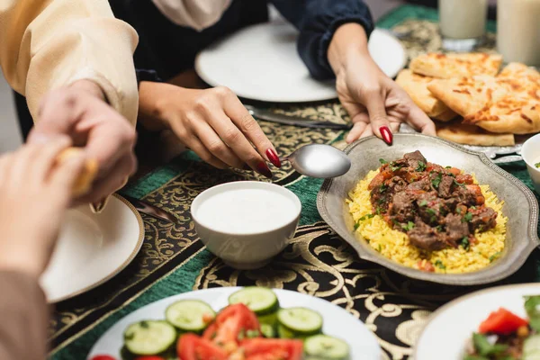 Vista recortada de la mujer musulmana poniendo pilaf en la mesa durante la cena de ramadán - foto de stock