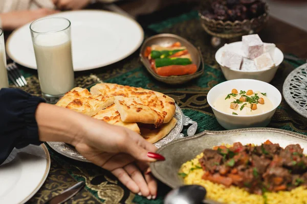 Vista recortada de la mujer musulmana poniendo comida sabrosa en la mesa durante la cena ramadán - foto de stock