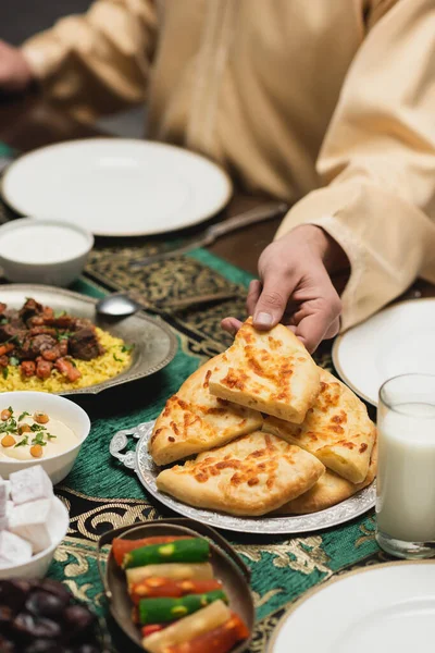 Vista recortada del hombre musulmán tomando pan de pita cerca de la comida durante la cena de ramadán - foto de stock