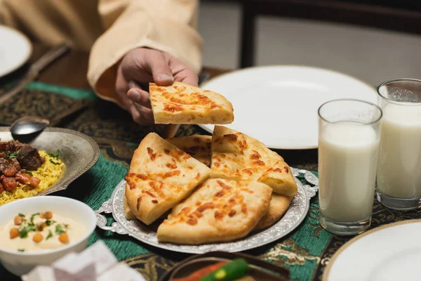 Vista recortada del hombre musulmán tomando pan de pita durante la cena de ramadán en casa - foto de stock