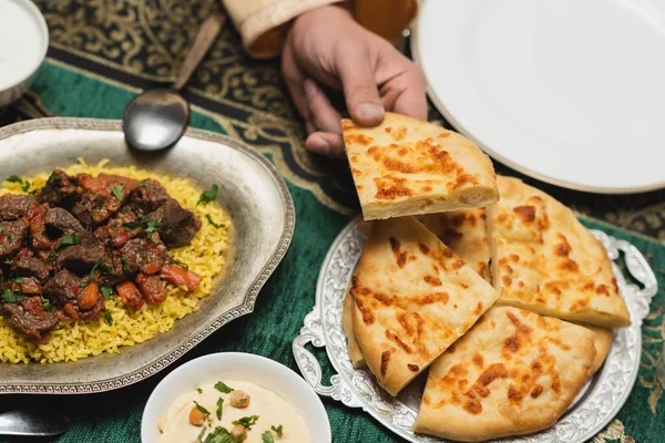 Cropped view of muslim man holding pita bread near pilaf on table at home — Stock Photo