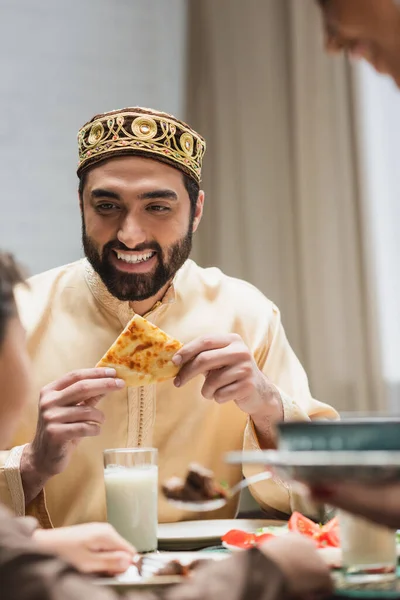 Smiling muslim father holding pita bread near blurred family during ramadan dinner — Fotografia de Stock