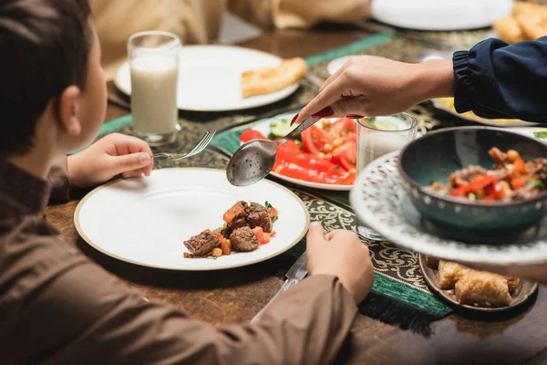 Muslim mother serving food on plate near son and ramadan dinner at home — Foto stock