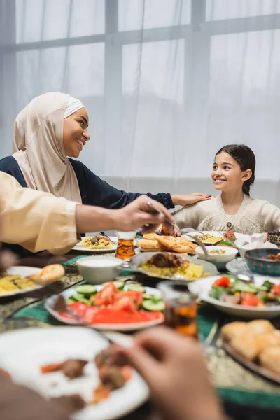 African american mother in hijab looking at daughter near ramadan dinner at home - foto de stock