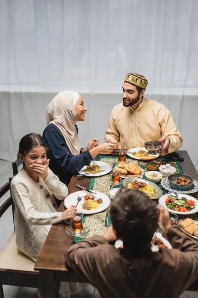 Padres musulmanes hablando cerca de niños y comida ramadán en casa - foto de stock
