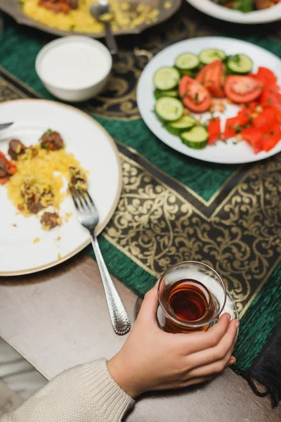 Vue du dessus de la fille musulmane tenant verre de thé turc près du dîner ramadan flou à la maison — Photo de stock