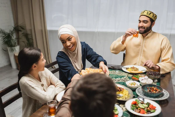 African american mother in hijab holding pita bread near family during ramadan — Foto stock