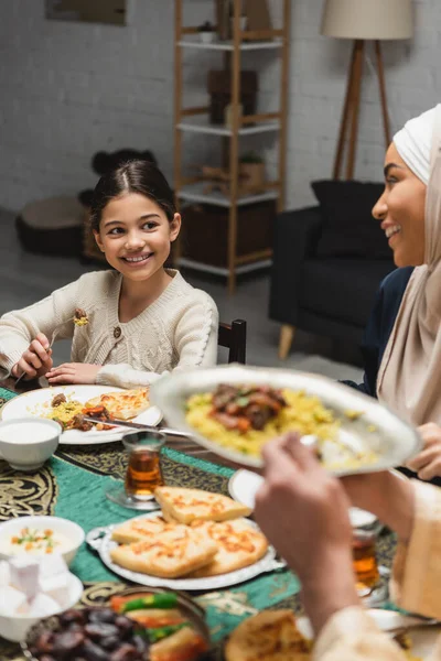 Lächelndes muslimisches Mädchen schaut Eltern beim Ramadan zu Hause beim Essen an — Stockfoto