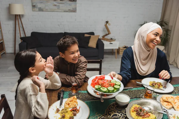 Веселые мусульманские дети разговаривают рядом с африканской американской мамой в хиджабе во время ифтара дома — стоковое фото