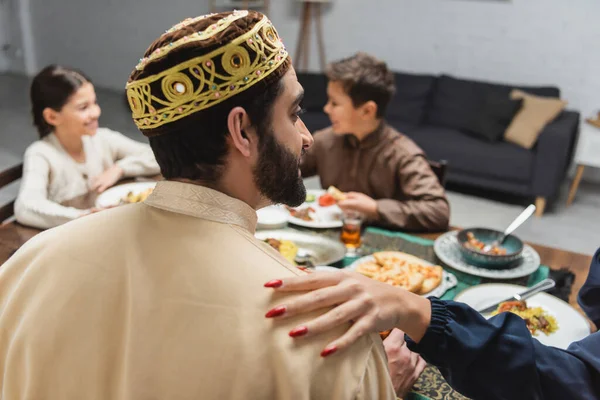 Muslim woman touching husband near blurred kids during iftar at home — Stockfoto