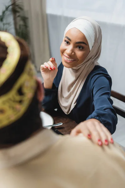 Smiling african american woman in hijab looking at blurred husband at home — Stock Photo