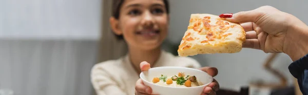 Muslim mother holding pita bread near blurred daughter with sauce at home, banner - foto de stock