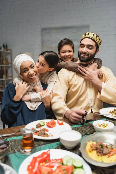 Alegre familia del Medio Oriente abrazándose cerca de la comida durante el ramadán en casa - foto de stock