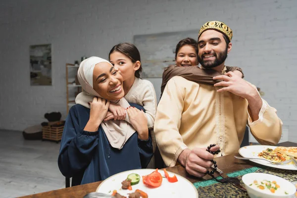Des enfants musulmans souriants embrassant les parents pendant le dîner du ramadan à la maison — Photo de stock
