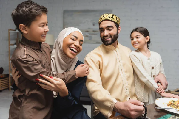 Cheerful middle east family hugging kids during dinner at home - foto de stock