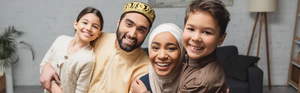 Веселые родители с Ближнего Востока и дети смотрят в камеру дома, баннер — стоковое фото