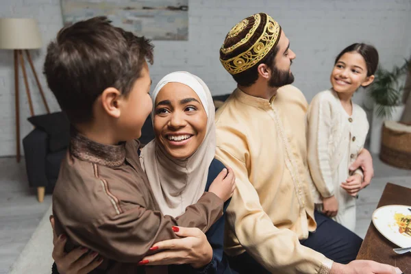 Smiling middle east parents hugging daughter and son during ramadan dinner at home - foto de stock