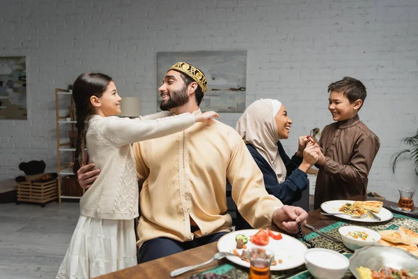 Cheerful middle eastern family hugging and talking during ramadan dinner at home - foto de stock