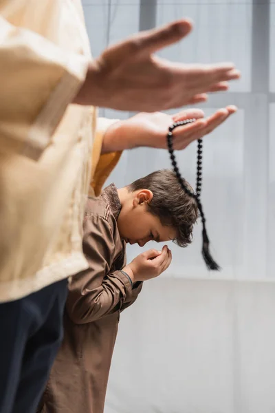 Middle eastern boy praying near father with prayer beads during ramadan at home — Stock Photo