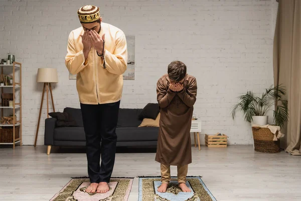 Barefoot muslim father and boy praying on rugs at home — Stock Photo