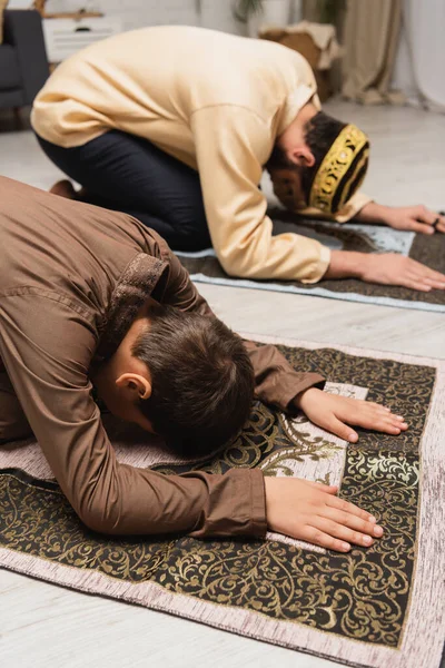 Muslim boy praying on rug near blurred father during ramadan — Foto stock