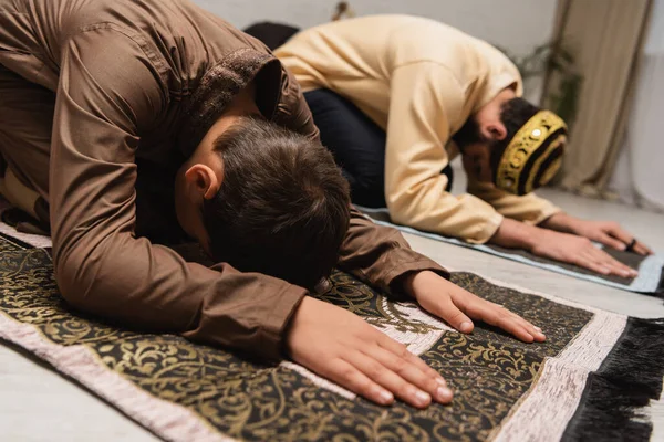 Muslim child praying on rug near father during salah at home — Stock Photo