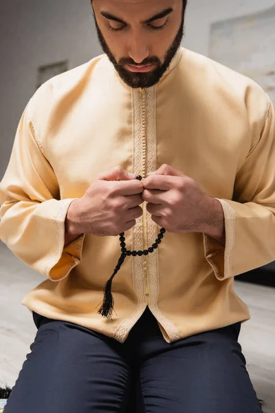 Bearded muslim man holding prayer beads during salah at home — Stock Photo