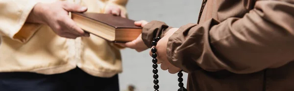 Cropped view of muslim father giving book to son with prayer beads at home, banner — Stock Photo