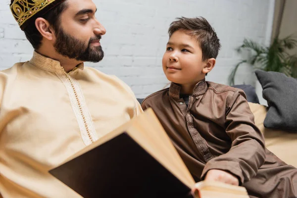 Garçon musulman regardant papa près du livre flou à la maison — Photo de stock