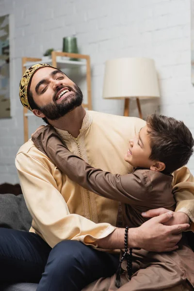 Smiling muslim child hugging father with prayer beads at home — Photo de stock