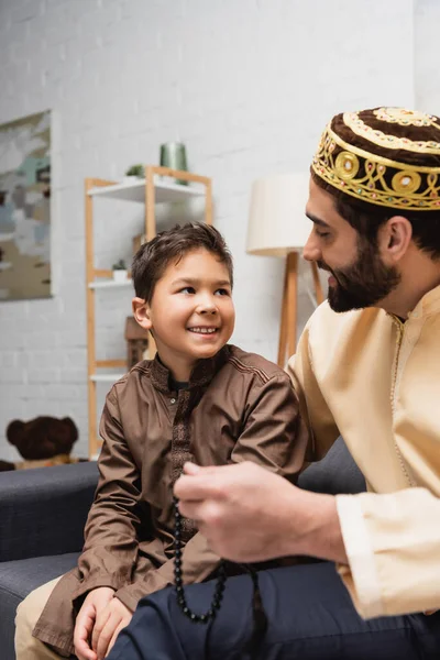 Smiling muslim boy looking at father with prayer beads at home — Stock Photo