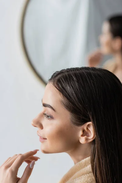 Side view of smiling young woman looking away near blurred mirror in bathroom — Stock Photo