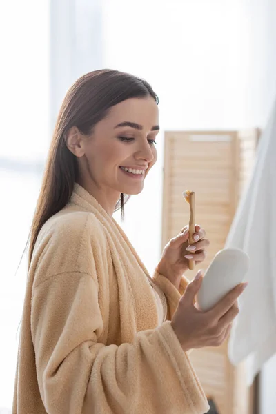 Felice giovane donna in possesso di spazzolino da denti e guardando tubo con dentifricio al mattino — Foto stock