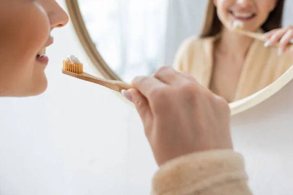 Vue recadrée de jeune femme heureuse brossant les dents près du miroir dans la salle de bain — Photo de stock