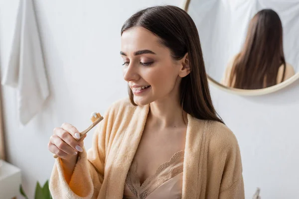 Молода і весела жінка в халаті дивиться на зубну щітку з зубною пастою — стокове фото