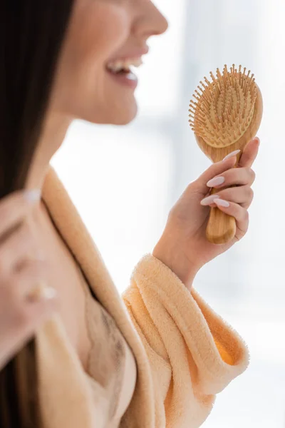 Обрізаний вид щасливої молодої жінки, що тримає дерев'яну щітку для волосся у ванній — стокове фото