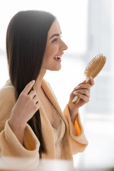 Side view of happy young woman holding wooden hair brush in bathroom — Stock Photo