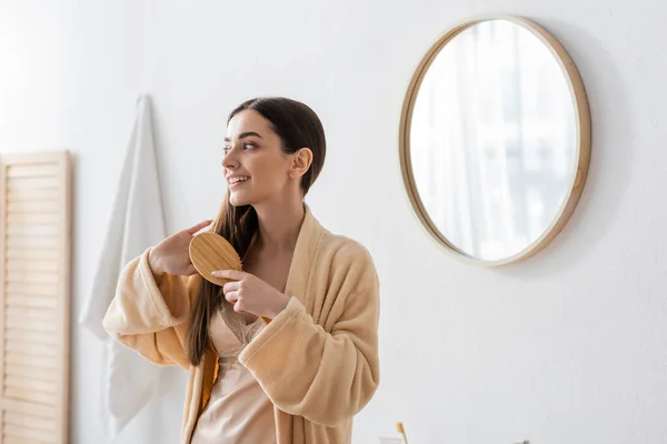 Glücklich junge Frau im Bademantel Bürsten der Haare in weißen modernen Badezimmer — Stockfoto