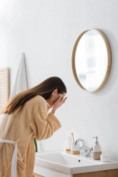 Jeune femme brune avec des cheveux longs lavage visage dans la salle de bain — Photo de stock