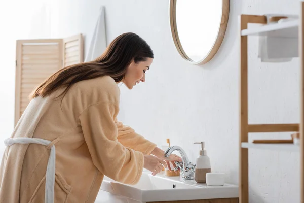 Vue latérale de la jeune femme brune aux cheveux longs ayant la routine du matin dans la salle de bain — Photo de stock