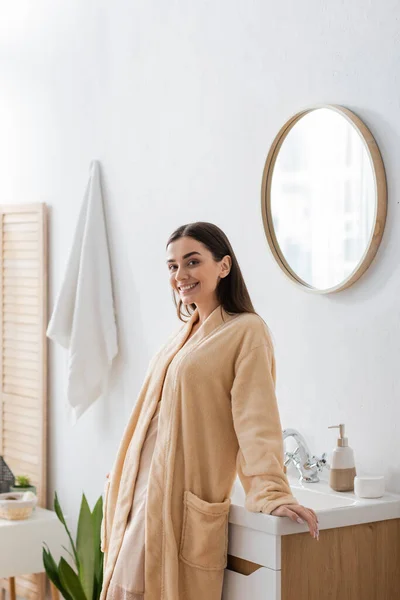 Young happy woman in bathrobe looking at camera in bathroom — Stock Photo